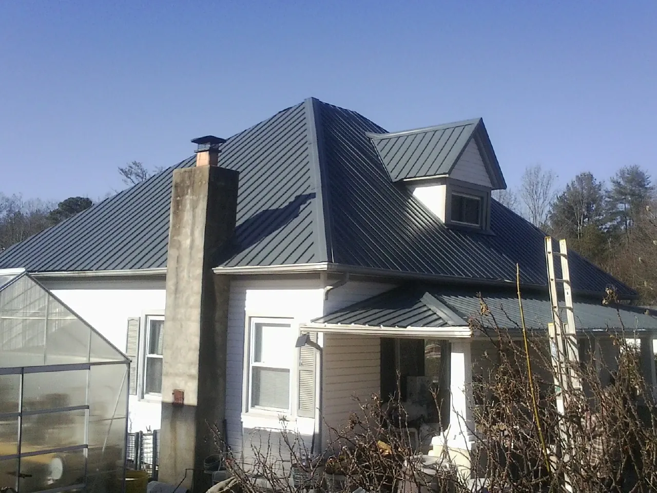 Dark blue standing seam metal roof on a white farmhouse with dormer — Slate & Tile Roof Repair by Roofing Brothers in Fort Lee