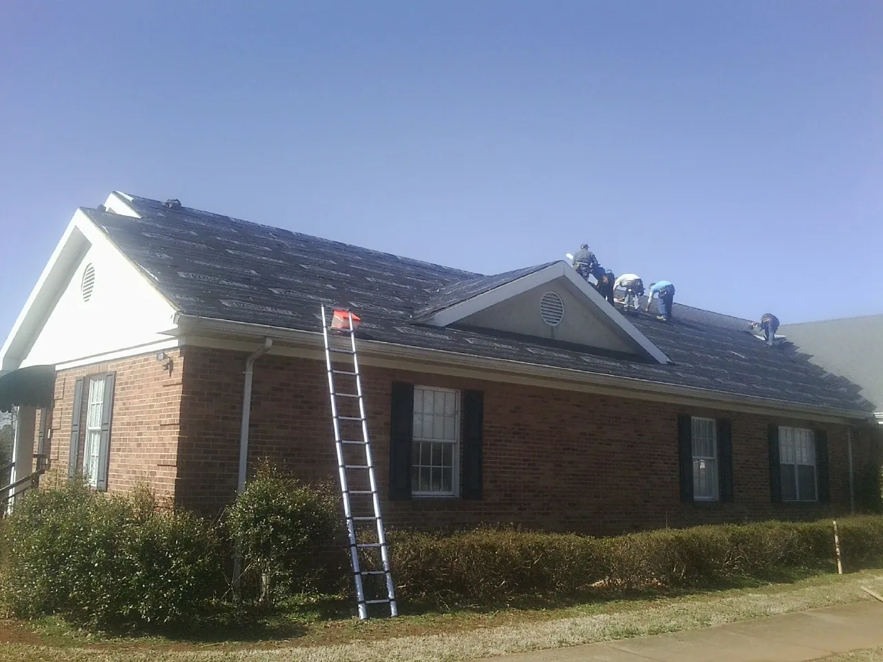 Crew tearing shingles off a brick ranch roof with a ladder set — Emergency Roof Repair work by our crew in Fort Lee