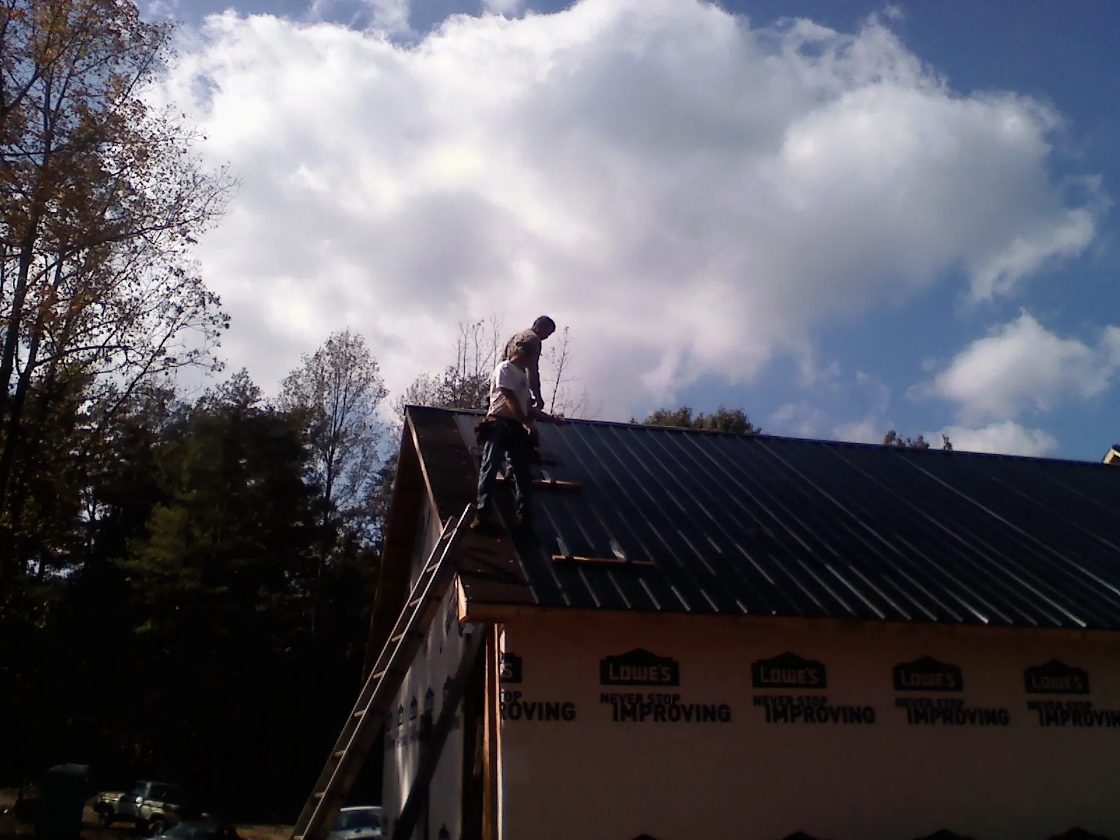 Roofer fastening dark metal panels high against a cloudy sky, from a Roof Inspection job in Fort Lee
