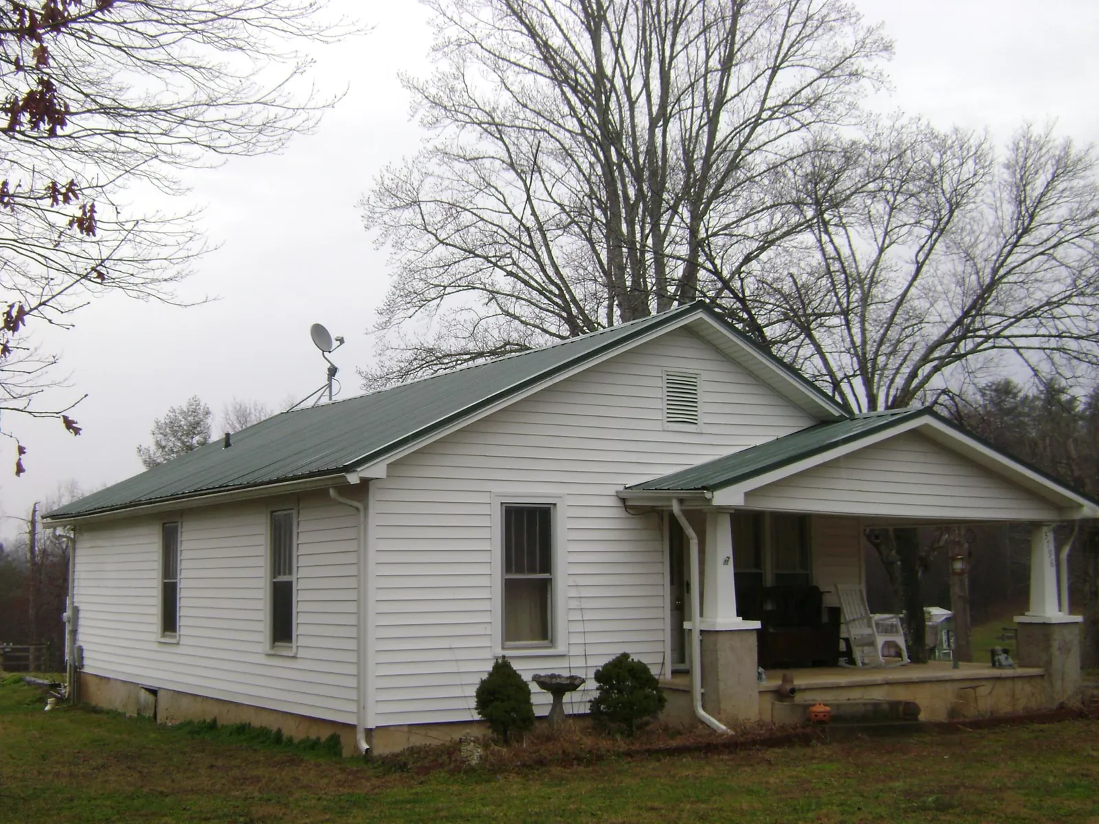 Green metal roof on a white bungalow with a side porch in Fort Lee