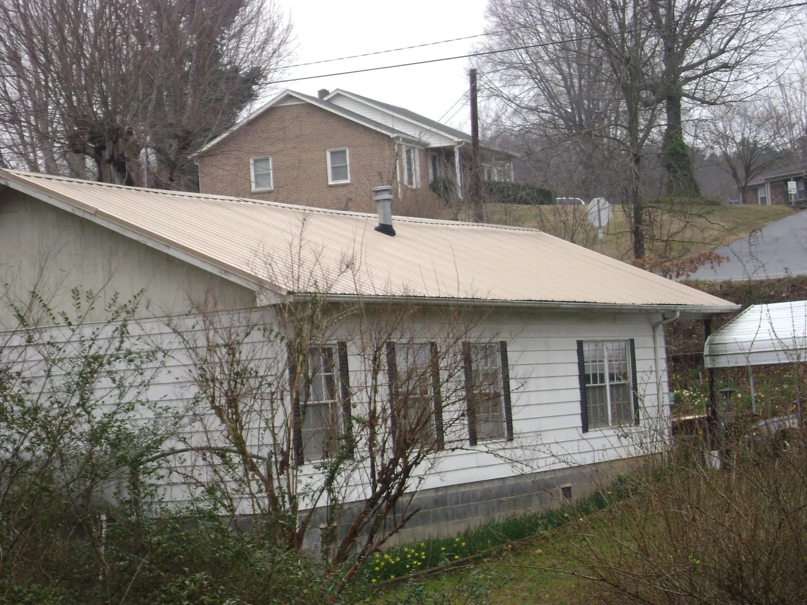 Tan metal roof on a white sided house set into a hillside — Commercial Roofing by Roofing Brothers in Fort Lee